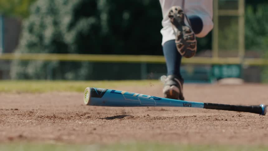 A baseball batter drops the bat and runs toward first base after a hit in slow motion