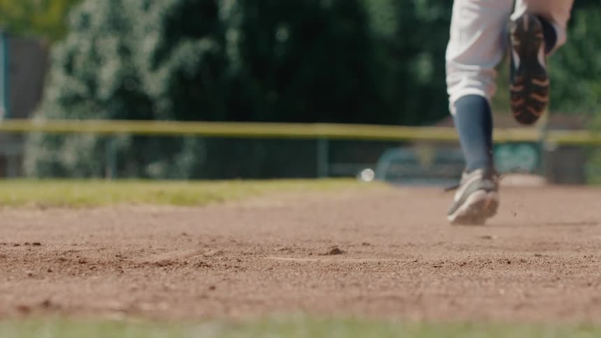 In dramatic slow motion, a baseball player's cleats tear through the dirt as they sprint from the base