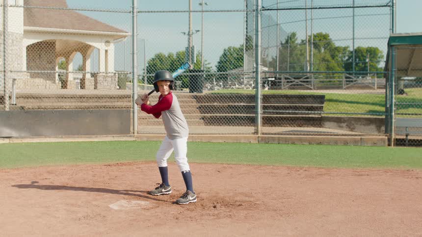 Young boy in a baseball uniform stands in the batter's box with a glowing bat in a still cinemagraph