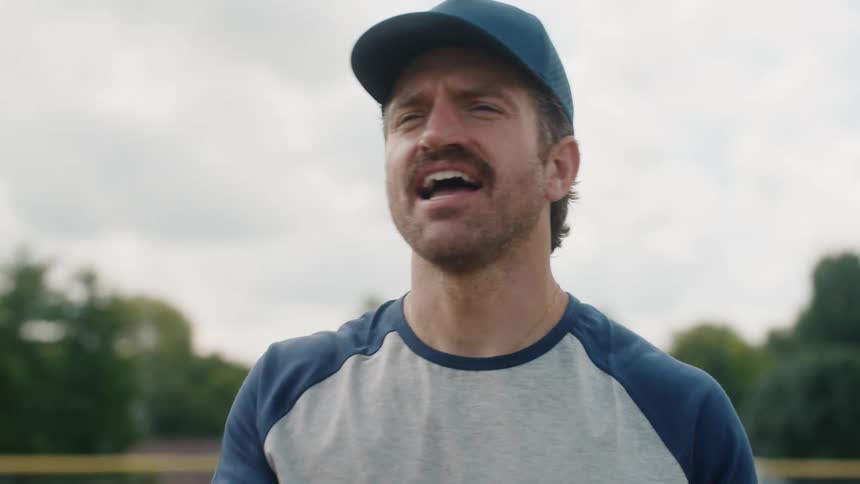 An enthusiastic baseball player with a mustache yells encouragement from the field during a game in slow motion
