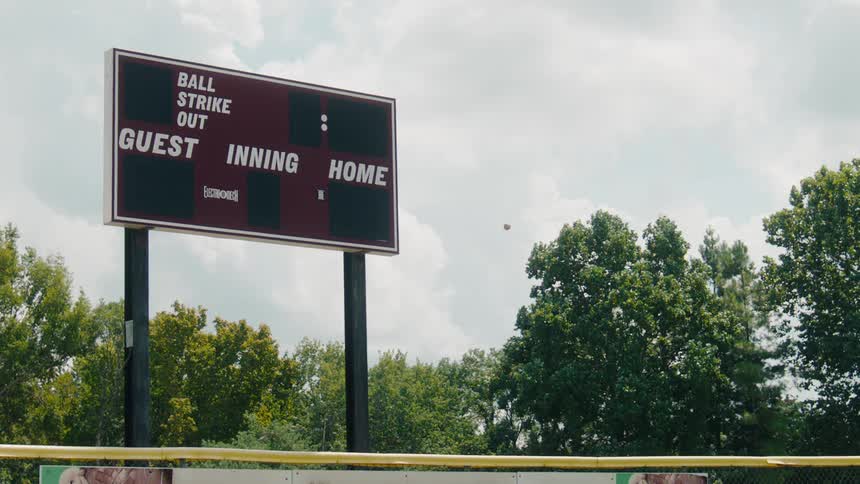 A baseball flies through the air in slow motion for a home run in front of a classic ballpark scoreboard