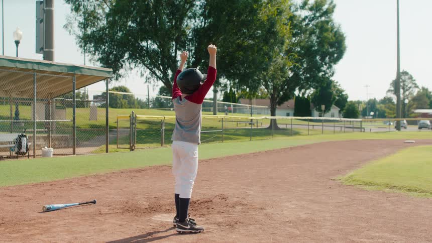 A young little league player runs to home plate and celebrates scoring a home run in slow motion