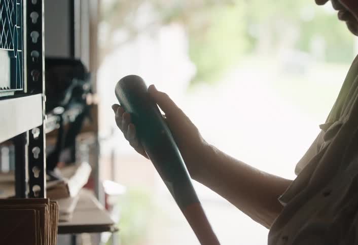 A person nostalgically holds an old baseball bat in a dimly lit garage, reflecting on memories