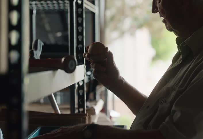 A senior man finds an old baseball in his garage and holds it in his hands, reminiscing about the past