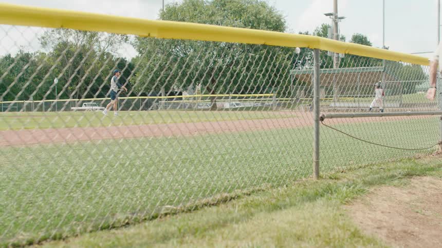 A man carries a bucket of baseballs to a baseball field where players are practicing in slow motion