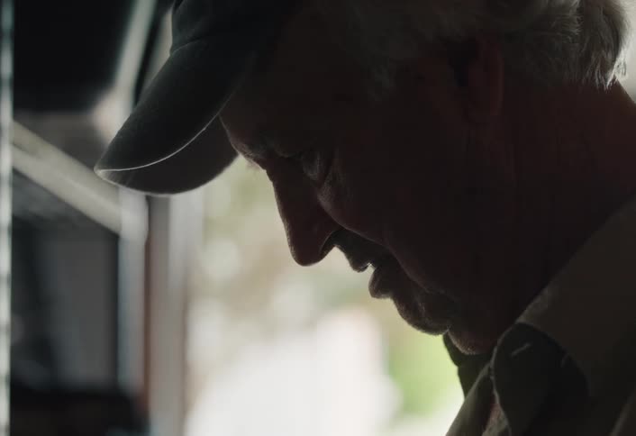 An older man in a hat is silhouetted as he fondly looks at an old baseball, reminiscing about past memories
