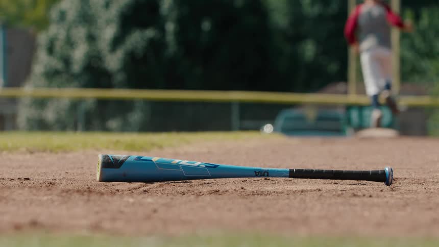 Slow motion shot of a baseball bat on the infield with a player running to a base in the background