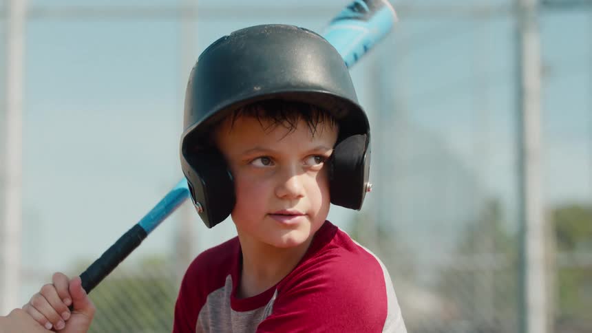 A determined young boy in a batting helmet swings a baseball bat in slow motion and runs towards first base on a sunny day