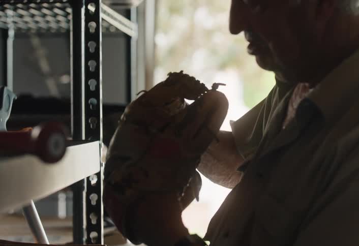 A senior man smiles fondly as he inspects an old, weathered baseball glove, reminiscing in his garage