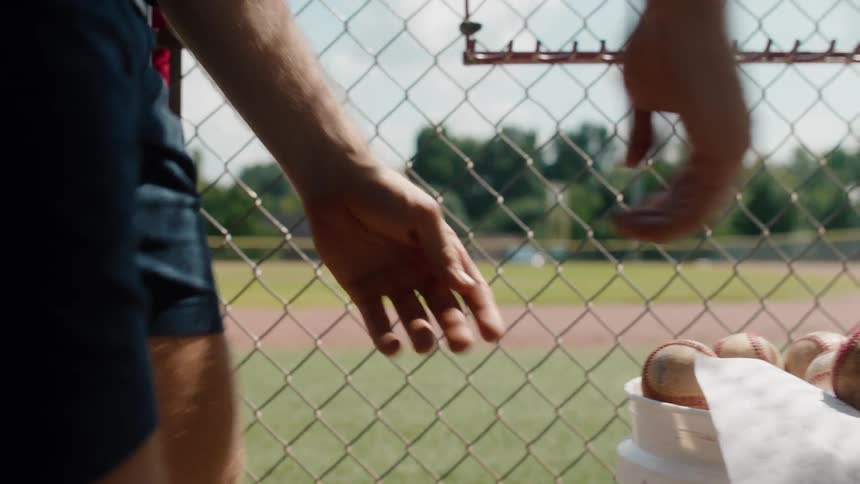 A slow motion shot of a baseball coach walking to the dugout where a young player meets him at the fence to review the game plan
