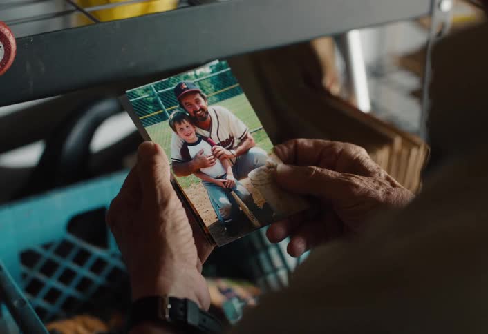A person looks through a crate of old keepsakes and reminisces over childhood baseball photos with their family
