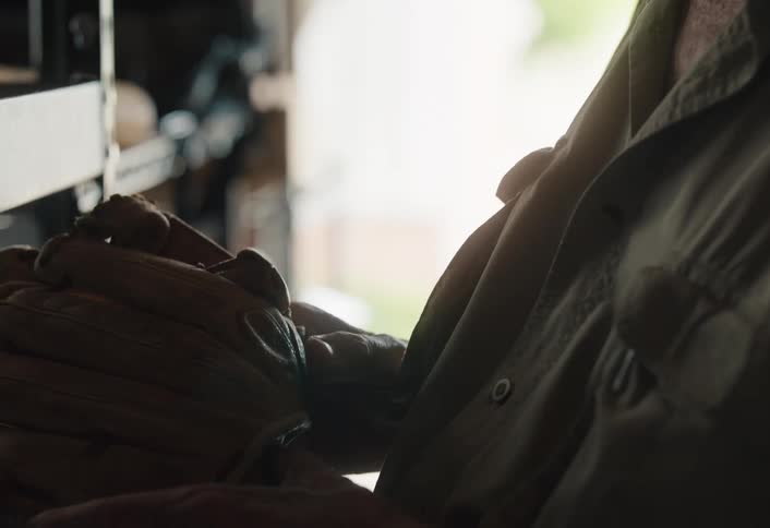 A close-up slow-motion shot shows an elderly man in a cap reminiscing with his old baseball glove before putting it away