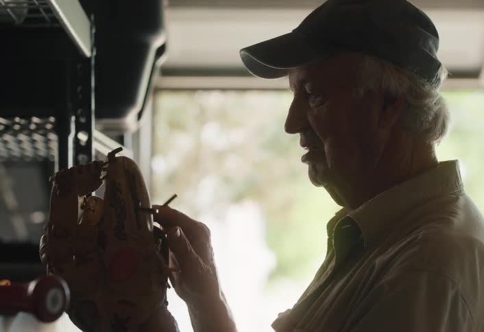 An elderly man fondly remembers his past while holding and examining an old baseball glove in his garage