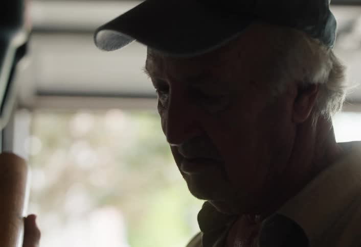 Close up of a nostalgic elderly man in a dark garage reminiscing as he looks over an old baseball bat