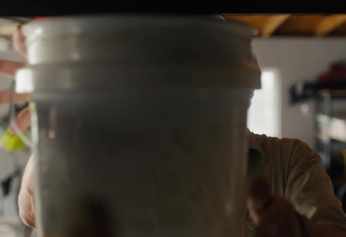 An elderly man in a baseball cap organizes items and moves boxes in his cluttered home garage