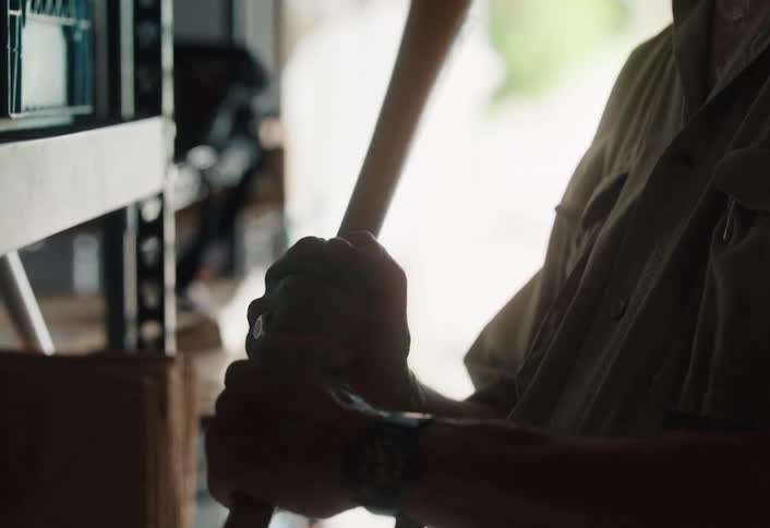 A sentimental elderly man in his garage smiles while holding an old wooden baseball bat, reminiscing about fond memories
