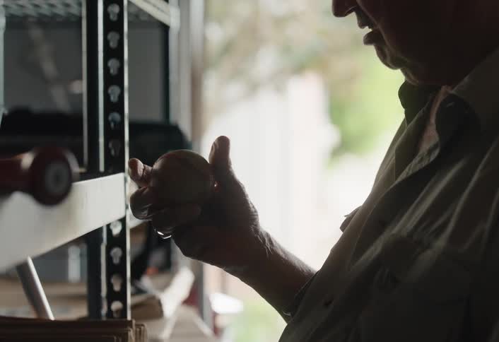 A nostalgic older man pulls a crate from a shelf in his garage and fondly examines an old, treasured baseball from his past