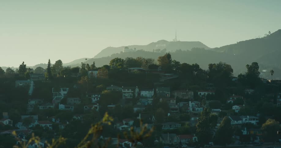 A hazy morning view of the Los Angeles hills with a helicopter flying past the iconic Hollywood sign and Griffith Observatory