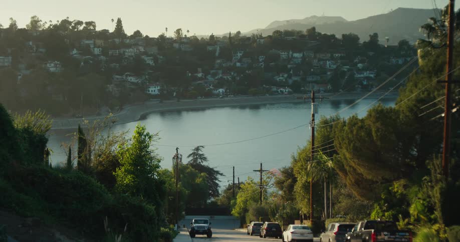 Scenic view from a tree-lined street overlooking the Hollywood Reservoir, with the iconic Hollywood sign visible in the distant hills