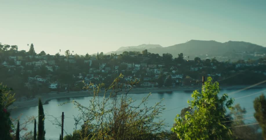 A scenic tilt-up shot reveals the Silver Lake Reservoir with the iconic Hollywood sign in the background on a hazy morning