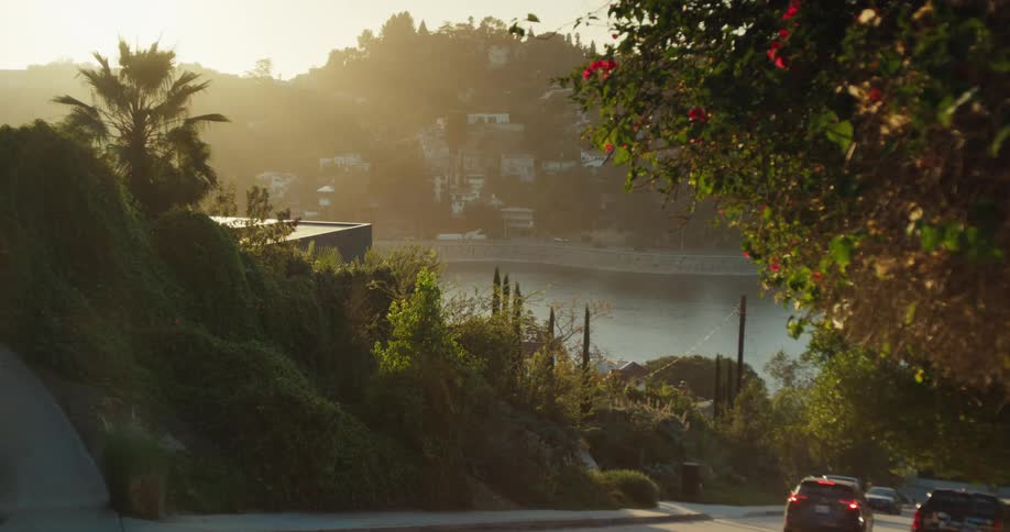 A picturesque view of the Hollywood Reservoir from a winding road as the golden hour sun casts a warm glow over the hills
