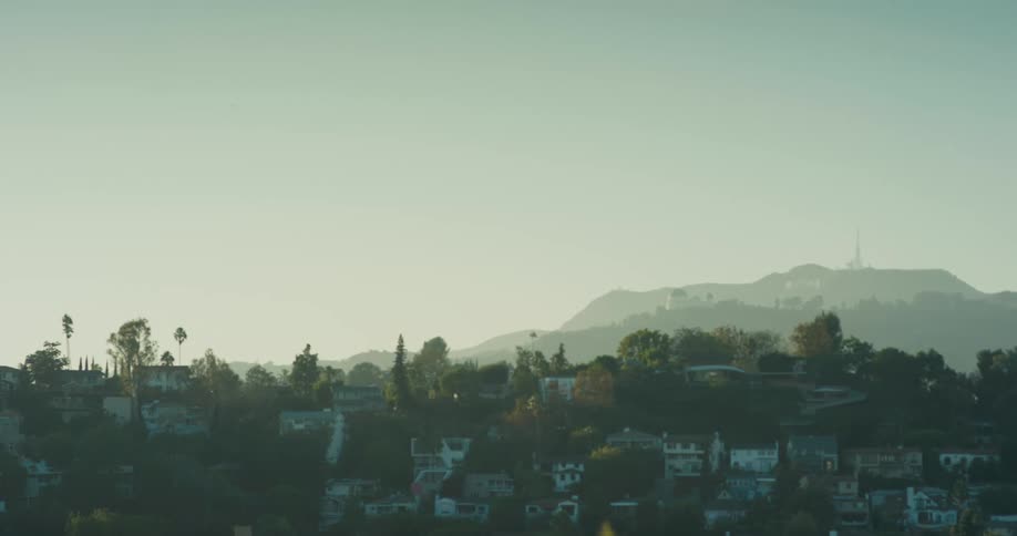 A static wide shot of the Hollywood Hills in Los Angeles, showing the iconic Hollywood sign in the hazy distance at sunrise