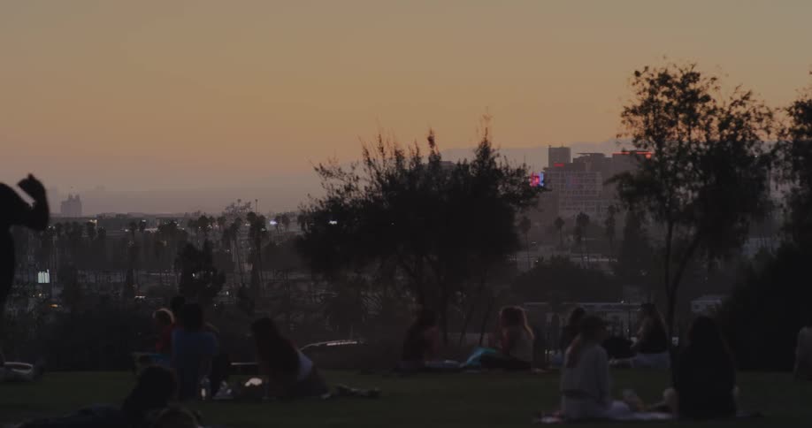 Silhouetted groups of people enjoying a picnic and relaxing in a city park at sunset