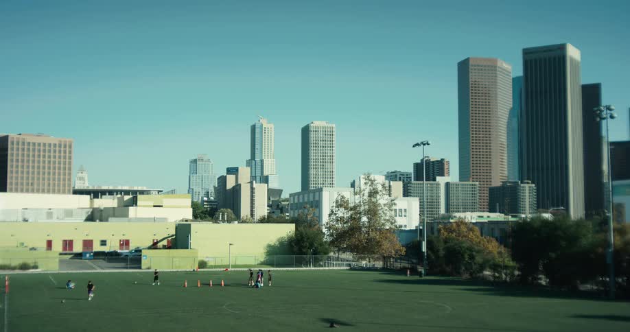 A soccer team runs drills on a vibrant green sports field set against the iconic backdrop of the downtown Los Angeles skyline