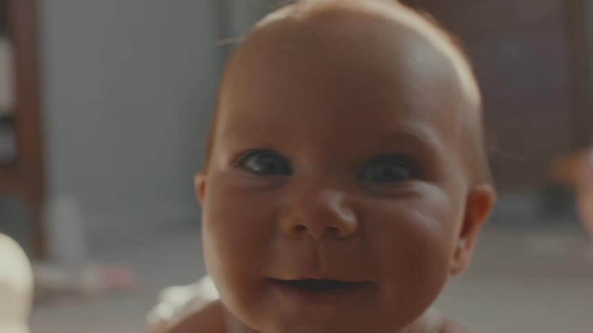A curious baby in slow motion crawls directly towards the camera, smiling in a sunlit room