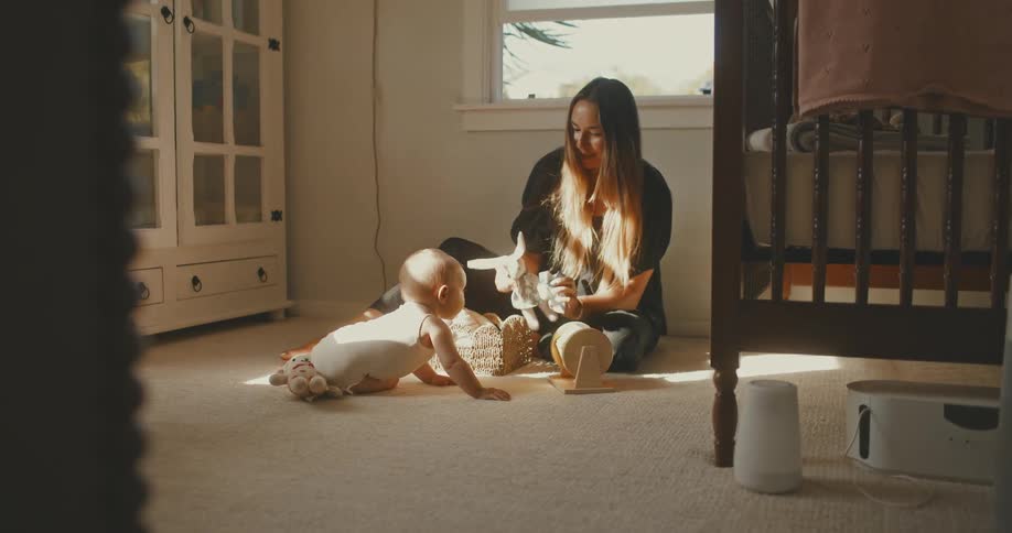 Mother and her curious baby play with toys on the floor of a warm, sunlit nursery
