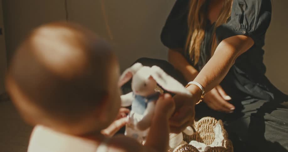 A loving mother plays with her baby boy with a stuffed bunny on the floor of a sunlit nursery