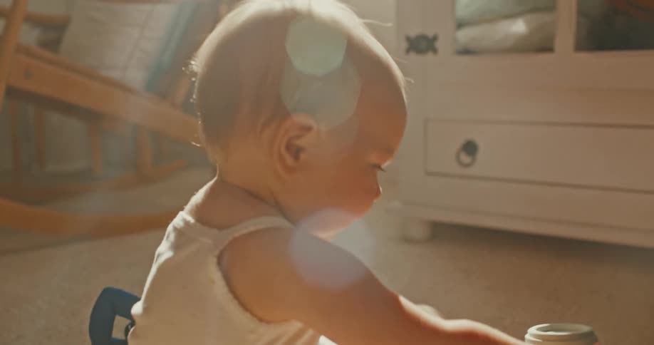 A smiling baby joyfully knocks over a tower of stacking cups while playing with a parent on the floor in a warm, sunlit room