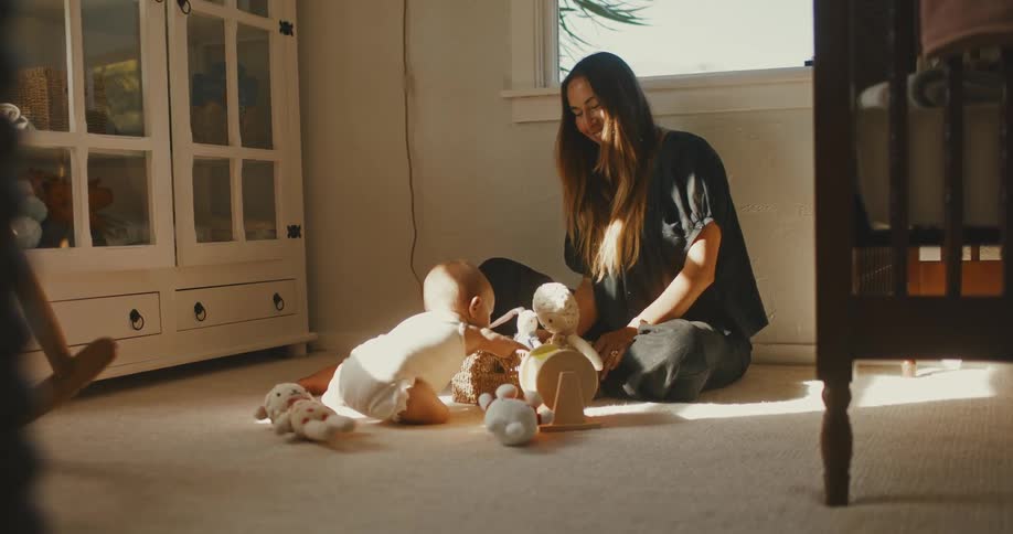 A loving mother and her adorable baby play with toys on the floor of a warm, sun-drenched nursery
