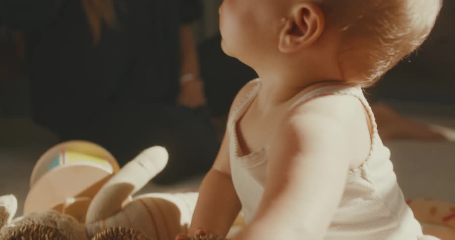 An adorable baby in a sunlit room chews on a book before playing with a basket of toys in slow motion