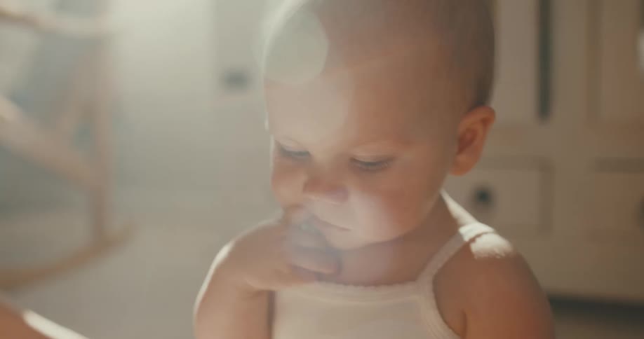 Close-up of a sweet baby with beautiful blue eyes sitting in a room filled with warm, soft sunlight