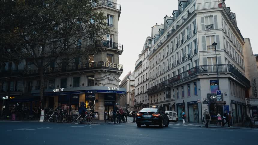 A black taxi waits at a classic Parisian street corner as pedestrians and bicyclists pass by