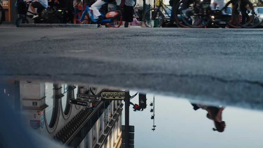 A Paris Metro sign reflects in a street puddle as a blur of cyclists and pedestrians move across the busy city intersection