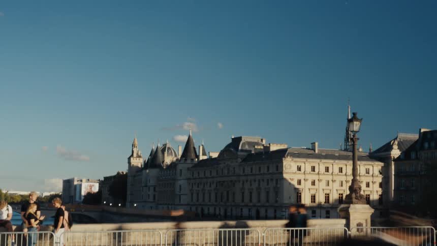 A sunny day time-lapse of blurred traffic passing a bridge in front of the historic Conciergerie building in Paris
