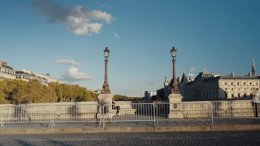 A sunny daytime timelapse captures the blurred motion of pedestrians and traffic on a historic bridge in Paris, France