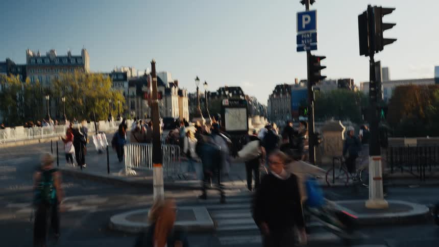 A motion-blur time-lapse of a bustling crowd of pedestrians crossing the street near the Pont Neuf bridge in Paris