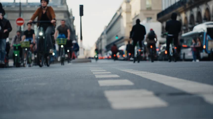Low-angle slow-motion shot of cyclists and scooter riders commuting down a busy city street