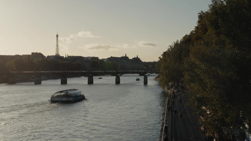 A tour boat cruises down the Seine River in Paris with the Eiffel Tower in the background during a beautiful sunset