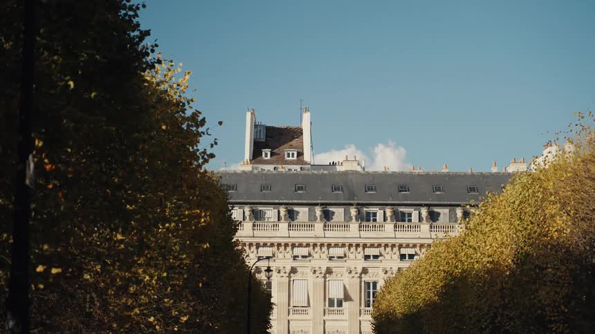 A stately Parisian building is framed by golden autumn trees on a bright, sunny day