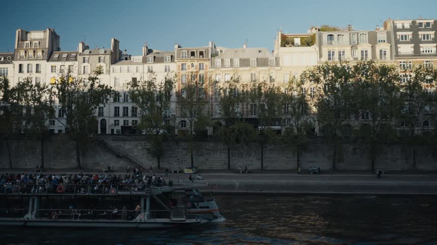 A Bateau Mouche tour boat full of passengers cruises down the Seine river in Paris on a sunny day