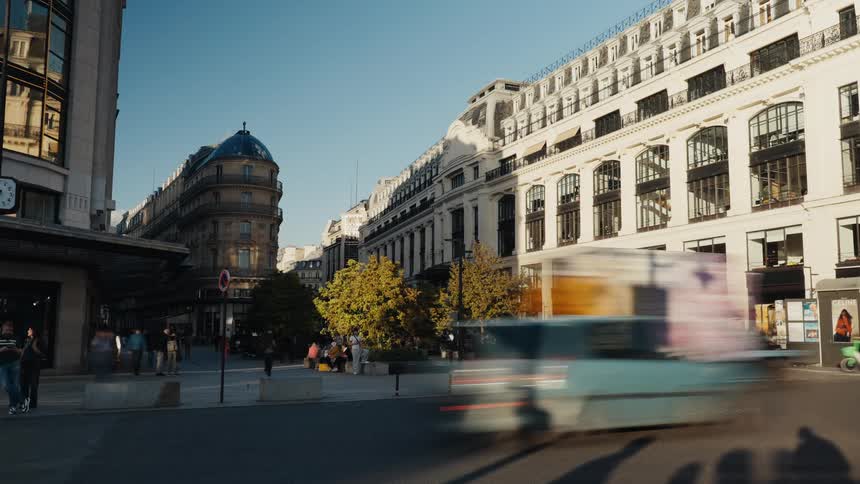 A dynamic timelapse captures the hustle and bustle of traffic and pedestrians on a sunlit street in Paris, France
