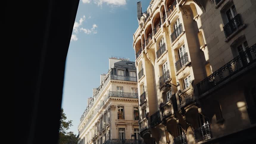 Sunlight illuminates the ornate facades of classic Parisian apartment buildings against a blue sky