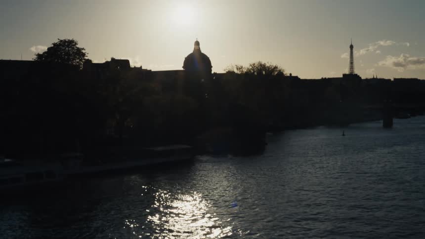A slow tilt up reveals the silhouetted Paris skyline and the Eiffel Tower over the Seine River at sunset