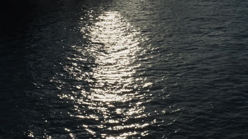 The sun's reflection shimmers and glitters on the surface of calm, dark water