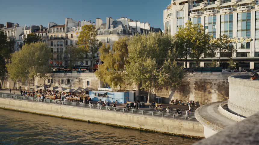 Parisians and tourists enjoy a sunny afternoon walking and relaxing at an outdoor cafe along the Seine River