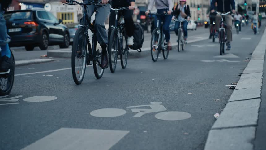 A slow-motion, low-angle view of diverse cyclists commuting on a dedicated bike lane in a bustling city